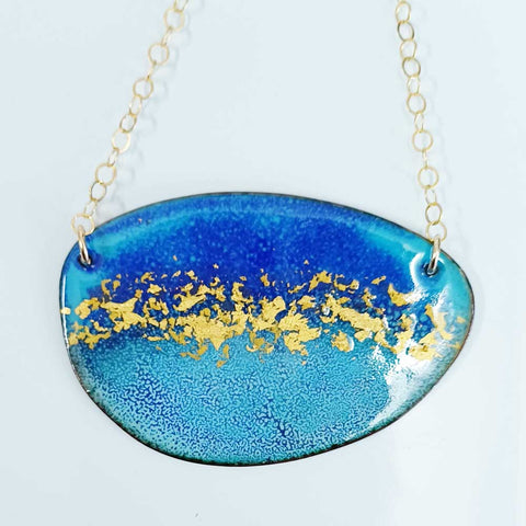 Oval shaped enamel pendant in dark and light blue with gold leaf particles decorating the middle of the shape. Gold plated chain with round likns is attached to either side with gold plated jumprings.