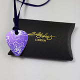 Front view of a purple Guitar pick pendant decorated with a delicate linear print in a silvery colour of larkspur flowers. The pendant has a purple satin ribbon and is placed upon a black pillow shaped box with the Sally Lees (London) logo in gold printed onto the box.