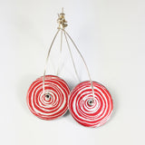 Women's suffrage reversible drop earrings showing the red sides. The earrings are made from disks with a printed end of scroll motif in silvery colour. The silver earring hoops are an eliptical shape and  each earring wire goes through a central hole in the disk.