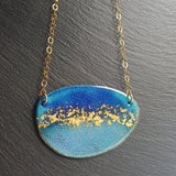 Oval shaped enamel pendant in dark and light blue with gold leaf particles decorating the middle of the shape. Gold plated chain with round likns is attached to either side with gold plated jumprings.