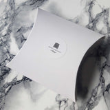 White pillow shaped gift box with Houses of Parliament logo in black type at the centre