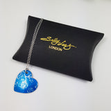 Blue heart shaped pendant with delicate linear drawing of sweet pea flowers with a siver chain. Displayed on a black pillow shaped box with a Sally Lees logo embossed in gold.