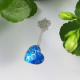 Blue heart pendant with linear print of sweet pea flowers. Pendant has a silver chain.