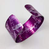 View of the open end of a cuff with dark magenta background with only the tail of a swallow and butterflies and delicate bird cage illustrations visible in a silvery colour. The butterflies overlap the bird cages and only a tail of a bird can be seen in this photograph. A portion of the inside of  the cuff can be seen and the Sally Lees logo can be seen on the inside surrounded by the butterflies and bird cage illustrations.