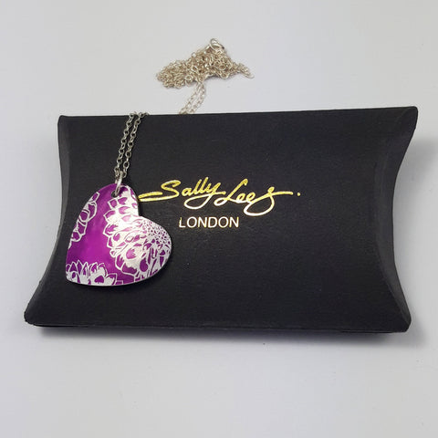 Anodised aluminum pink pendant with aster flower print in silvery colour displayed on a black pillow shaped box with gold 'Sally Lees' logo on the middle of the box.