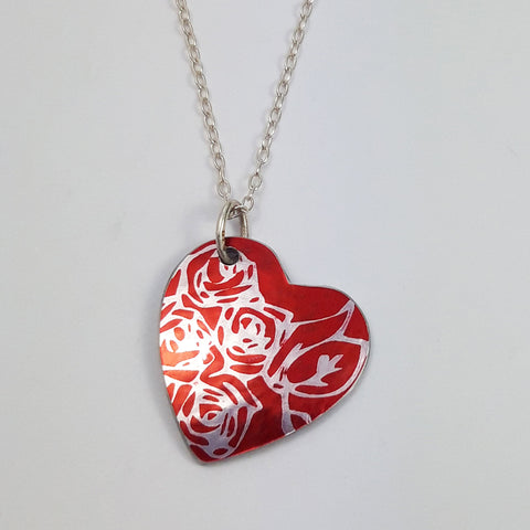 red  heart pendant with silvery rosespattern and silver chain on a white back ground