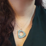 Green side of reversible triangular women's suffrage pendant with rounded edges and circular hole in the middle hung on a silver chain with a silver jump ring shown on a model