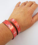 Anodized aluminum wrap around cuff in citrus orange with silvery coloured printed floral pattern on wrist of adult women