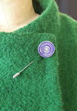 Purple 'New Dawn' suffragette aluminum and silver pin on green coat lapel