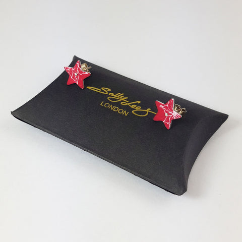 Red star poinsettia stud earrings for December birthdays displayed on a black pillow style box with a gold logo.
