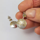 Hand crafted silver and gold etched round drop earrings held in a hand