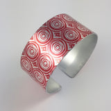 New Dawn Women's Suffrage cuff with a silver and red concentric circles patterns two across with a silvery coloured inside.