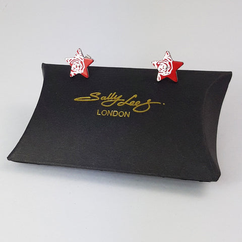 Red aluminium star studs decorated on the side of each one with a silvery linear pattern of abstracted roses. Displayed on a black pillow shaped box with a gold Sally Lees (London) logo.